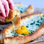 a hand dipping dough in an egg Khachapuri Adjaruli